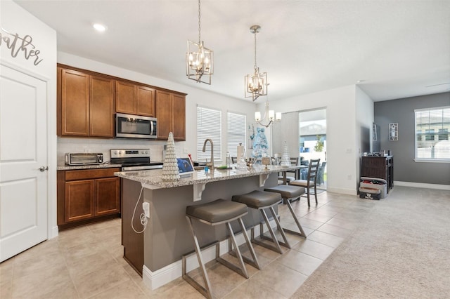 kitchen with light stone countertops, decorative light fixtures, a kitchen island with sink, a breakfast bar, and appliances with stainless steel finishes