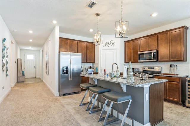 kitchen with a center island with sink, sink, light stone countertops, appliances with stainless steel finishes, and a kitchen bar