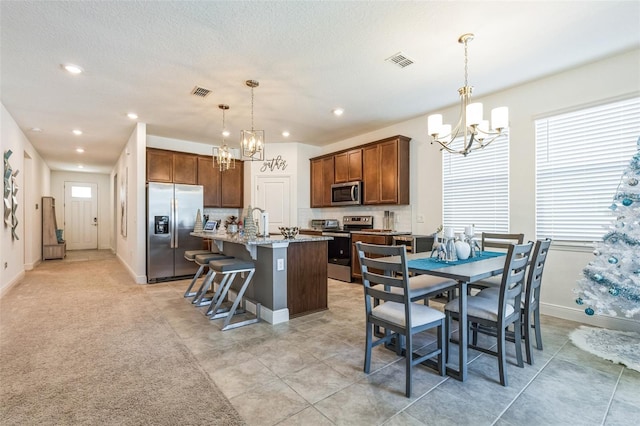 kitchen featuring light stone countertops, appliances with stainless steel finishes, a kitchen island with sink, decorative light fixtures, and a chandelier