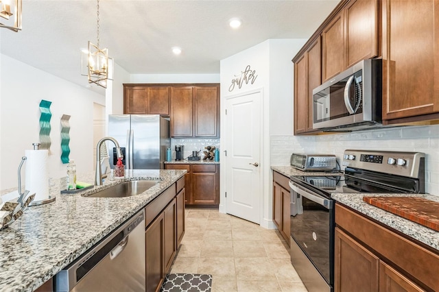 kitchen featuring light stone countertops, appliances with stainless steel finishes, sink, an inviting chandelier, and hanging light fixtures