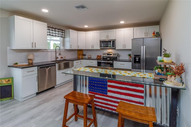 kitchen with appliances with stainless steel finishes, light hardwood / wood-style floors, white cabinetry, and sink