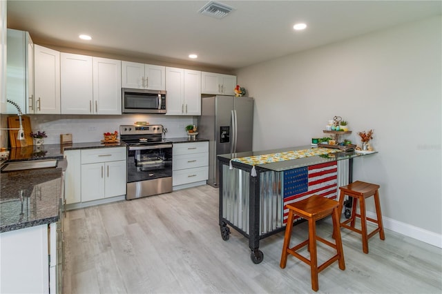 kitchen featuring white cabinets, appliances with stainless steel finishes, light wood-type flooring, and tasteful backsplash