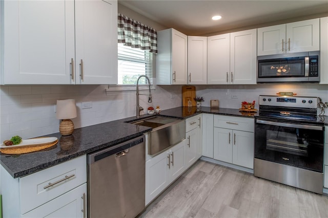 kitchen featuring white cabinets, stainless steel appliances, light hardwood / wood-style floors, and dark stone countertops