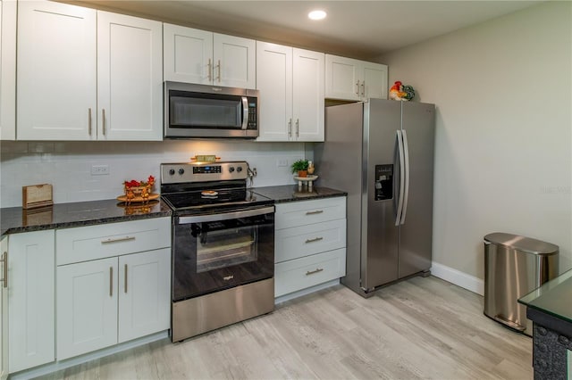 kitchen featuring tasteful backsplash, stainless steel appliances, dark stone countertops, light hardwood / wood-style floors, and white cabinetry