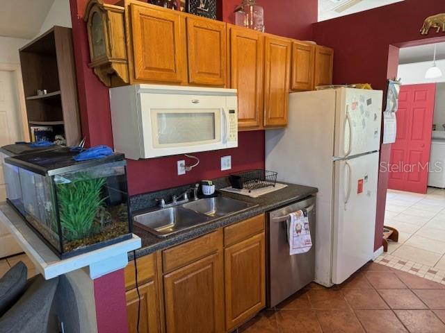 kitchen featuring tile patterned flooring, lofted ceiling, white appliances, and sink