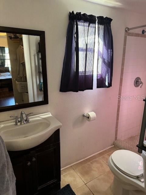 bathroom featuring a tile shower, tile patterned flooring, vanity, and toilet