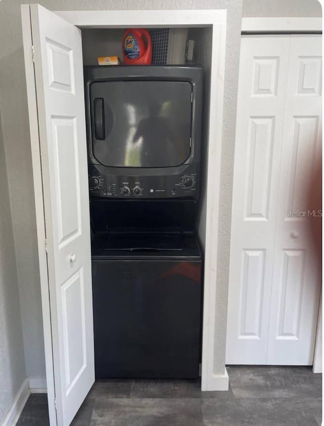 clothes washing area featuring stacked washer and dryer and dark wood-type flooring