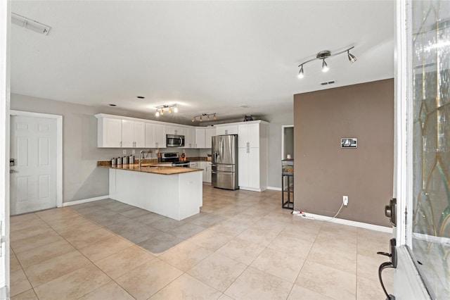 kitchen featuring kitchen peninsula, light tile patterned floors, white cabinetry, stone counters, and appliances with stainless steel finishes