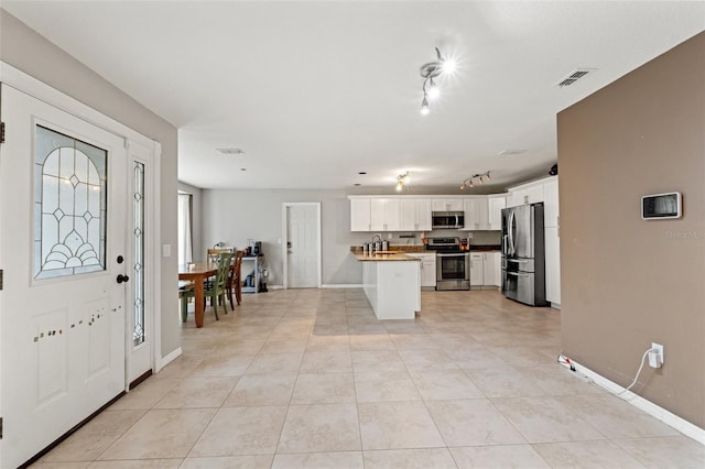 kitchen featuring kitchen peninsula, light tile patterned floors, white cabinets, appliances with stainless steel finishes, and sink