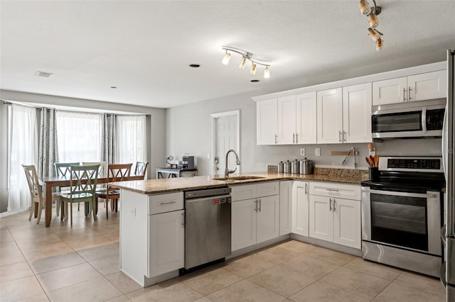 kitchen with sink, white cabinetry, kitchen peninsula, dark stone counters, and appliances with stainless steel finishes