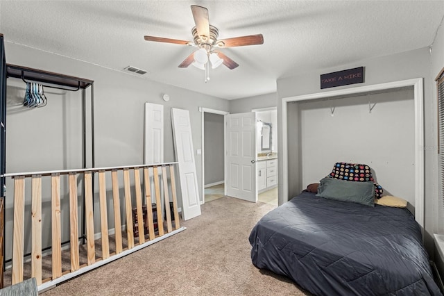 carpeted bedroom featuring ceiling fan, ensuite bathroom, a closet, and a textured ceiling