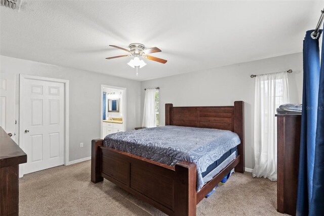 bedroom with ceiling fan, light colored carpet, and connected bathroom