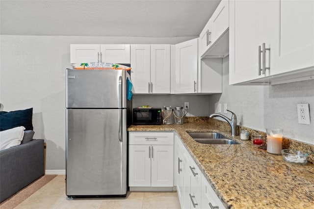 kitchen with stainless steel fridge, light stone counters, sink, white cabinetry, and light tile patterned flooring