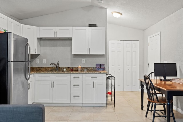 kitchen featuring lofted ceiling, white cabinetry, and stainless steel fridge