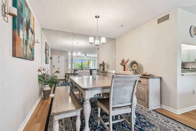 dining space featuring an inviting chandelier, a textured ceiling, and light hardwood / wood-style flooring