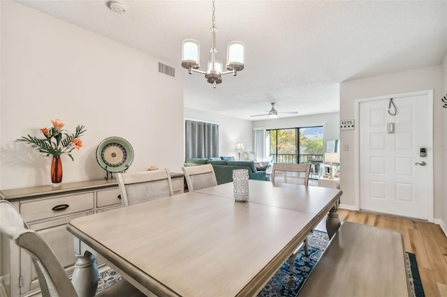 dining space with a textured ceiling, ceiling fan with notable chandelier, and light wood-type flooring