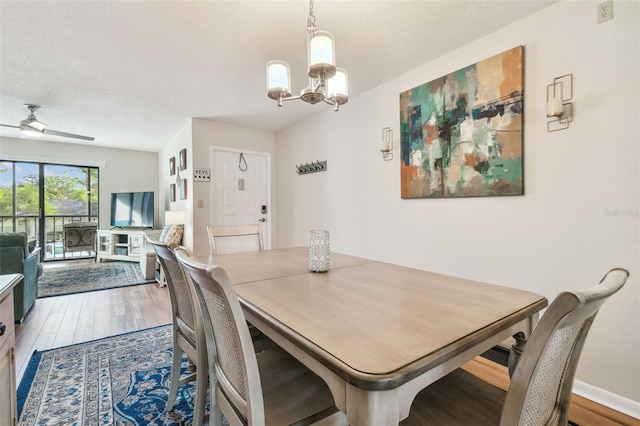 dining space with hardwood / wood-style flooring, ceiling fan with notable chandelier, and a textured ceiling