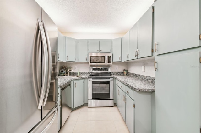 kitchen with appliances with stainless steel finishes, a textured ceiling, sink, gray cabinets, and light tile patterned flooring