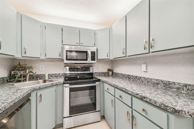 kitchen with sink, backsplash, a textured ceiling, light tile patterned flooring, and appliances with stainless steel finishes