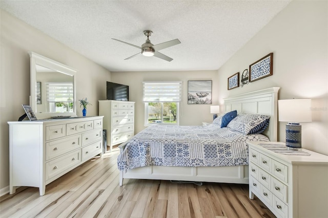 bedroom featuring ceiling fan, light hardwood / wood-style floors, a textured ceiling, and multiple windows