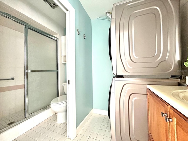 bathroom featuring vanity, tile patterned floors, toilet, stacked washing maching and dryer, and a shower with shower door