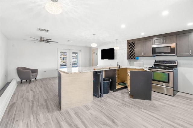 kitchen with light stone countertops, light wood-type flooring, stainless steel appliances, pendant lighting, and a kitchen island