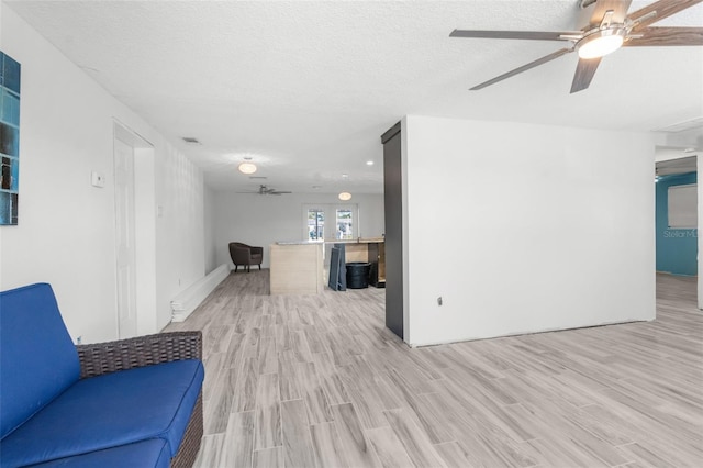 living room with ceiling fan, a textured ceiling, and light wood-type flooring