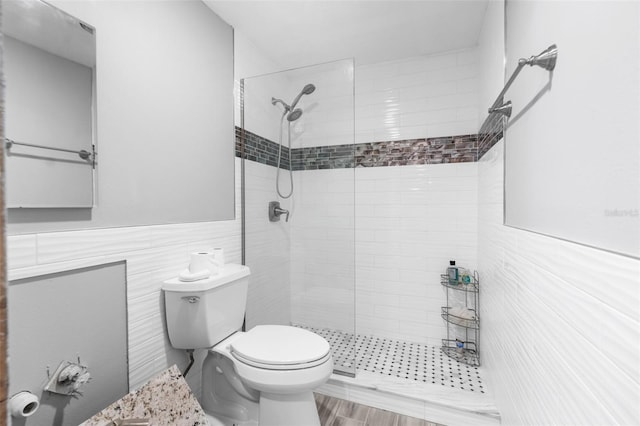 bathroom featuring a tile shower, toilet, tile walls, and hardwood / wood-style floors