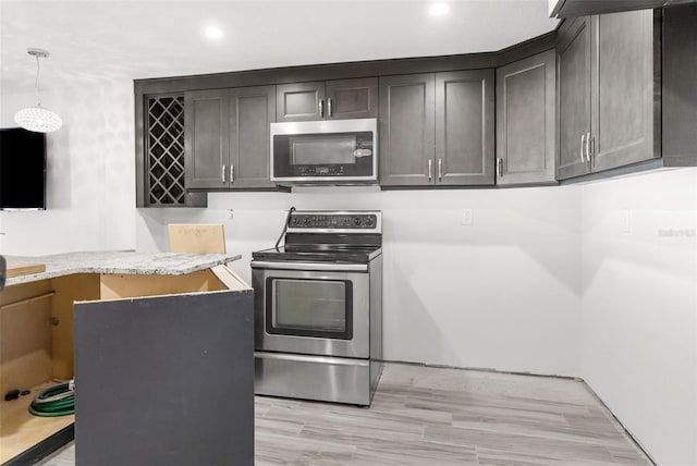 kitchen with appliances with stainless steel finishes, light wood-type flooring, dark brown cabinets, and pendant lighting