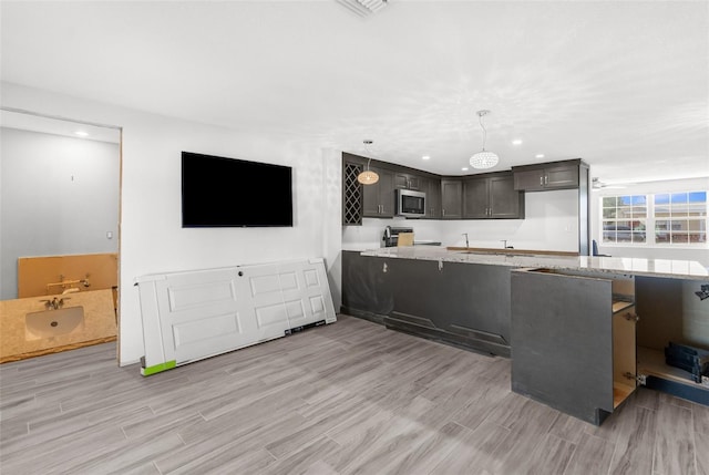 kitchen featuring hanging light fixtures, light wood-type flooring, appliances with stainless steel finishes, dark brown cabinets, and kitchen peninsula