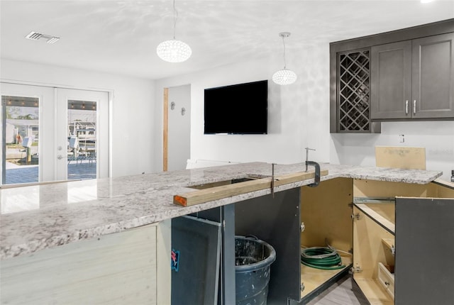 kitchen with pendant lighting, french doors, dark brown cabinets, light hardwood / wood-style floors, and light stone counters