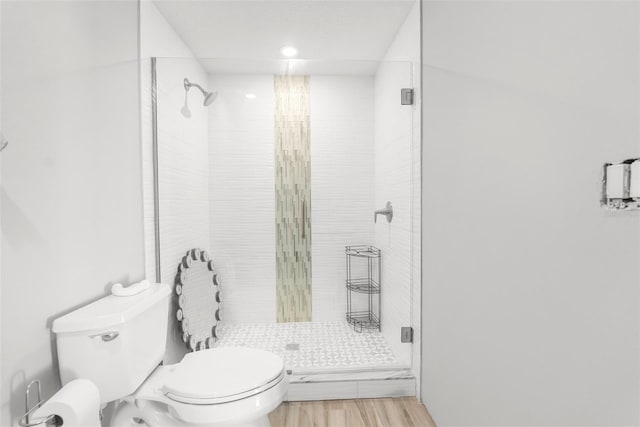 bathroom with hardwood / wood-style floors, a shower with door, and toilet