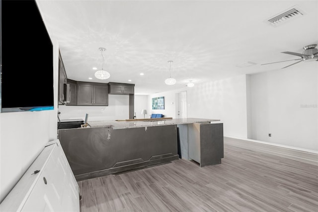 kitchen featuring kitchen peninsula, light hardwood / wood-style floors, dark brown cabinetry, and hanging light fixtures