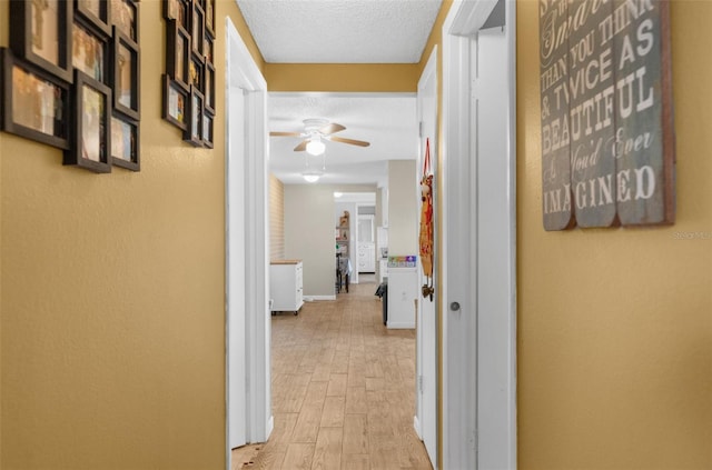 corridor with a textured ceiling and light wood-type flooring