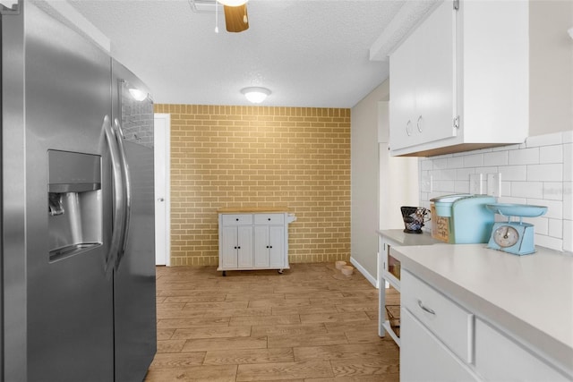 kitchen with tasteful backsplash, light wood-type flooring, white cabinets, stainless steel fridge, and a textured ceiling