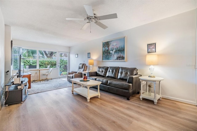 living room featuring ceiling fan, light hardwood / wood-style flooring, and a textured ceiling