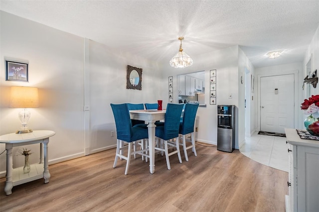 dining space featuring light hardwood / wood-style flooring, a textured ceiling, and an inviting chandelier