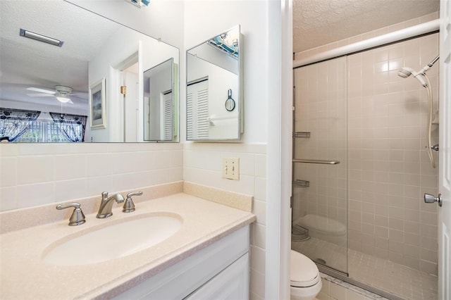 bathroom with a textured ceiling, toilet, a shower with door, vanity, and tile walls