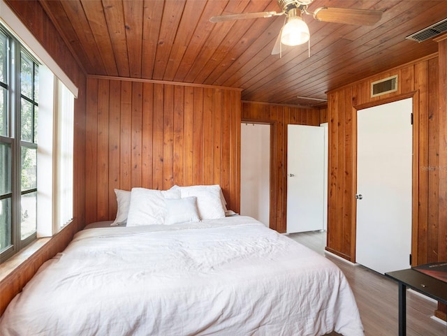 bedroom featuring ceiling fan, hardwood / wood-style flooring, multiple windows, and wood walls