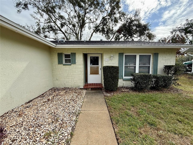 8704 Winding Wood Dr, Port Richey, FL 34668 - doorway to property featuring brick siding, a lawn, and stucco siding