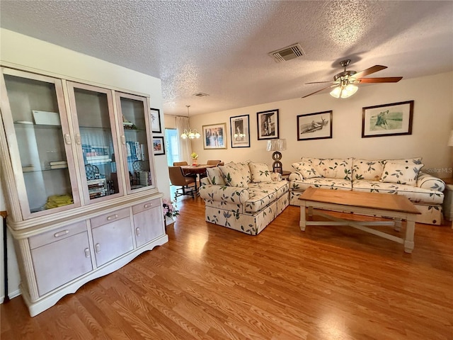 living room featuring ceiling fan with notable chandelier, light wood-type flooring, and a textured ceiling