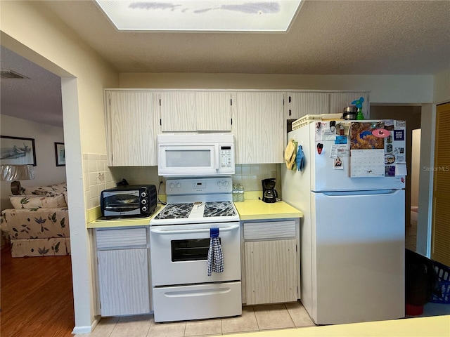 kitchen with a textured ceiling, light wood-type flooring, white appliances, and backsplash