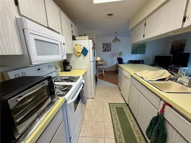 kitchen with light brown cabinetry, a textured ceiling, white appliances, sink, and light tile patterned flooring