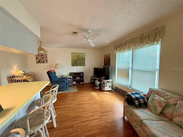 living room with ceiling fan, a textured ceiling, and hardwood / wood-style flooring