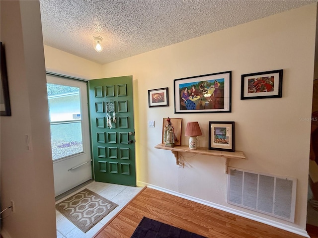 foyer with wood finished floors, a textured ceiling, baseboards, and visible vents