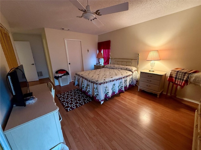 bedroom with a textured ceiling, visible vents, a ceiling fan, and wood finished floors