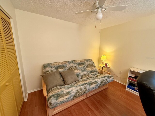 living area featuring baseboards, wood finished floors, ceiling fan, and a textured ceiling