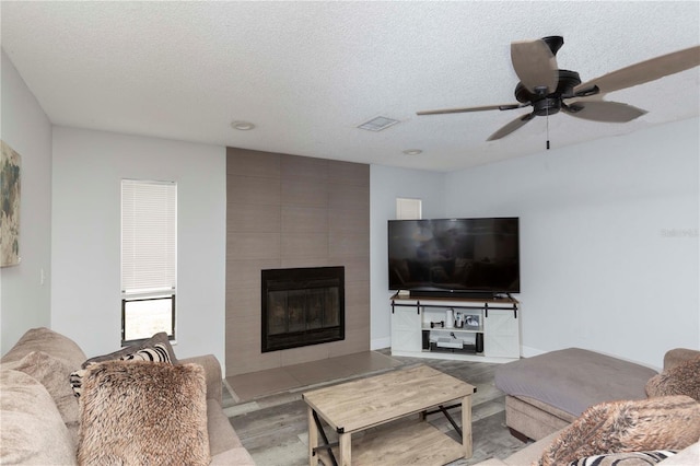 living room featuring a textured ceiling, ceiling fan, light hardwood / wood-style floors, and a fireplace