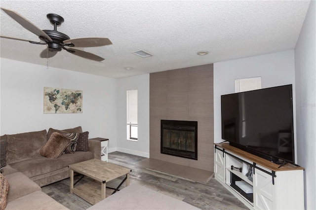 living room with a tile fireplace, ceiling fan, a textured ceiling, and hardwood / wood-style flooring