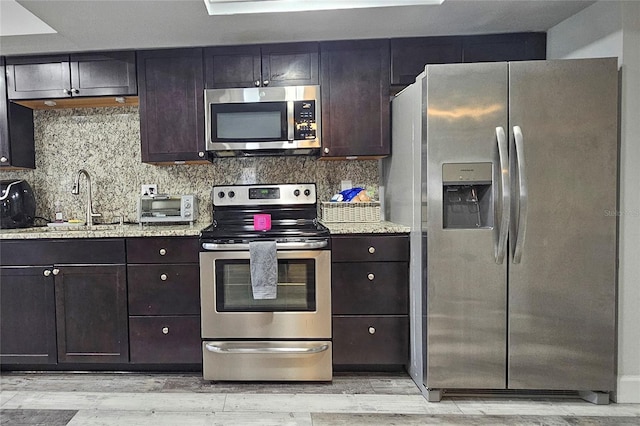 kitchen featuring light stone counters, light wood-type flooring, dark brown cabinetry, and appliances with stainless steel finishes